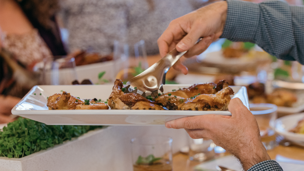 People pass a dish of chicken to one another during dinner.