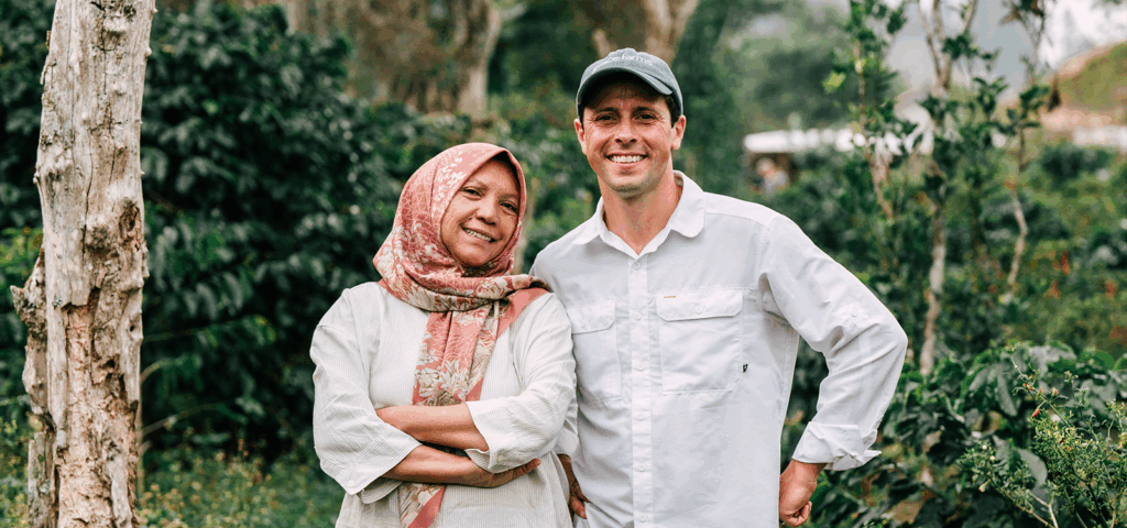 A woman and man stand in a field of coffee bean plants.
